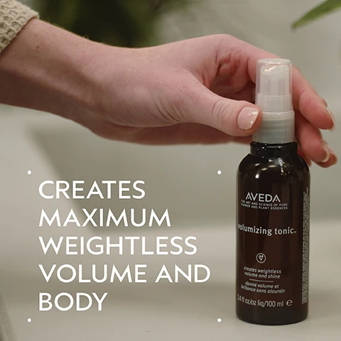 Image 2 - A persons hand holds a dark brown Aveda Volumizing Tonic spray bottle, with text on the bottle stating Aveda The Art and Science of Pure Flower and Plant Essences, volumizing tonic, creates weightless volume and shine, donne volume et brillance sans alourdir, 3.4 fl oz/oz liq/100 ml e, and large white text on the image left reads Creates Maximum Weightless Volume and Body. Image 3 - A split image displays a woman with long, red, wavy hair, labeled BEFORE on the left where her hair appears less defined and unwashed, and AFTER on the right where her hair is visibly more voluminous and defined after treatment, with additional text Unwashed Hair and Results with Damage Remedy™ Restructuring Shampoo and Conditioner, Daily Hair Repair, Volumizing Tonic and Light Elements™ Texturizing Cream. Blow dried with diffuser attachment. Image 4 - A dark green background features a circular cut-out showing close-up dry wheat stalks, with the text ALOE & WHEAT and HELP BUILD BODY AND ADD SHINE. Image 5 - A four-step hair care guide on a dark green background titled HOW TO USE features four circular images corresponding to text descriptions: 01 CLEANSE showing a person washing hair with foamy shampoo for Damage Remedy™ Restructuring Shampoo; 02 CONDITION with a hand squeezing white conditioner into a palm for Damage Remedy™ Conditioner; 03 TREAT displaying a hand holding an Aveda Damage Remedy Daily Hair Repair tube for Damage Remedy™ Daily Hair Repair; and 04 STYLE with a hand holding an Aveda Volumizing Tonic spray bottle for Volumizing Tonic and Light Elements™ Defining Whip. Image 6 - Numerous transparent water droplets of various sizes are scattered across a white background with a dark green border. Image 7 - Three white logos are displayed over a background of green leaves and a red plant, reading 100% VEGAN with a large V symbol, Certified B Corporation, and Cruelty Free INTERNATIONAL with a leaping rabbit symbol.